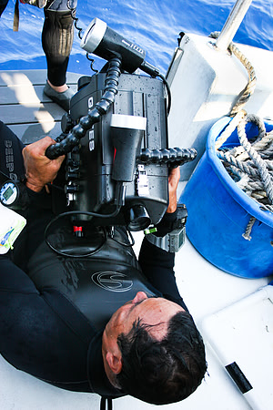 Man with an underwater housing and video camera, videoing a diver on a rebreather about to enter the water.