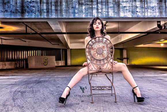 Erotic fashion nude photo of a woman nude in a public parking garage, flashing her pussy.
