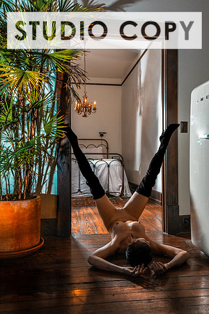 Erotic glamour photo of a hot woman in thigh-high boots, laying on the floor with her legs up and spread wide upon a doorframe