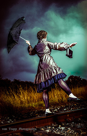 Stylized photo of a woman in a rainstorm with an umbrella balancing on a railroad track set agents dramatic clouds.