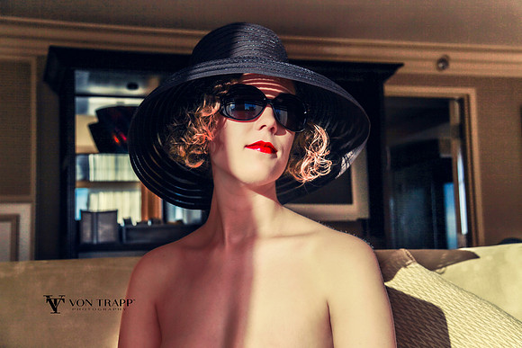 Implied nude of woman wearing a large-brim black hat.
