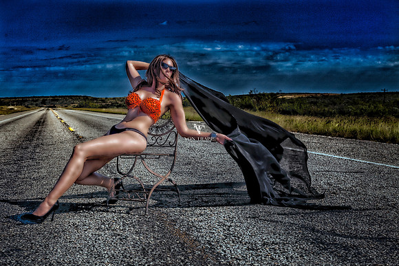 Glamour photo of a hot woman in a sexy bikini, sitting in a chair on a West Texas road.