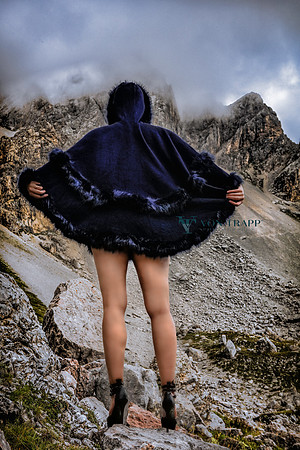 Provocative photo of a leggy semi-nude woman in stilettoes and a short cape photographed high in the Dolomite mountains.