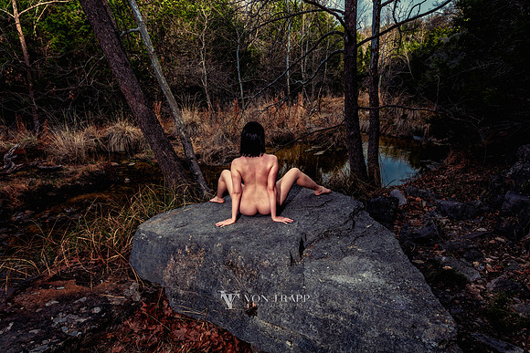 Art nude photograph of a hot woman along a river sitting with her legs spread.