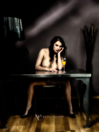 Photo of a nude woman sitting in a chair at a table in dramatic light.