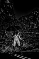 Art nude photo of a woman holding an umbrella, wearing thigh high boots, straddling the centerline of a highway in southwest desert of Texas.