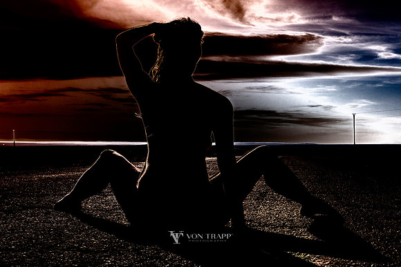 Sexy art nude photograph of a woman in silhouette sitting on the centerline of a hi way with her legs spread open. Erotic art nude.