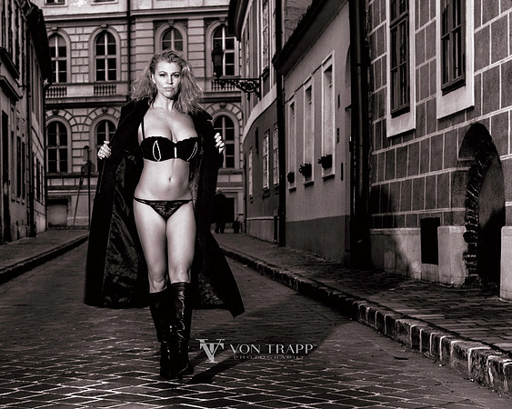 Photo of a woman wearing lingerie and a long coat walking on a cobbled street in Budapest.