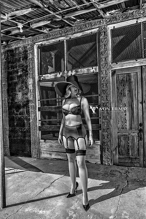 Black and white fashion-glamour photo of a hot woman outdoors in bra, garter belt, stockings ,broad brim hat and come fuck me stilettoes, flashing her pussy in public.