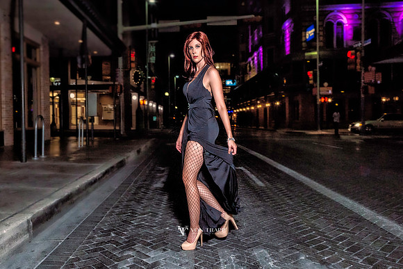 Photo of a hot redhead in a long gown with a high slit  wearing fishnets and come fuck me heels, crossing a street at night in San Antonio.