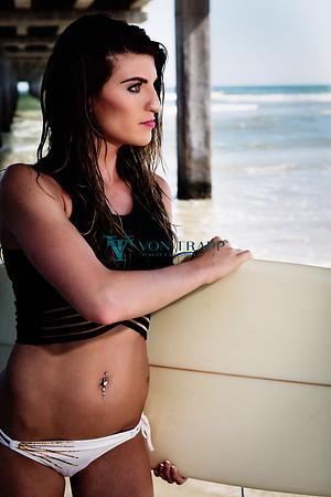Woman with a thruster surfboard under a pier in Port Aransas Texas.