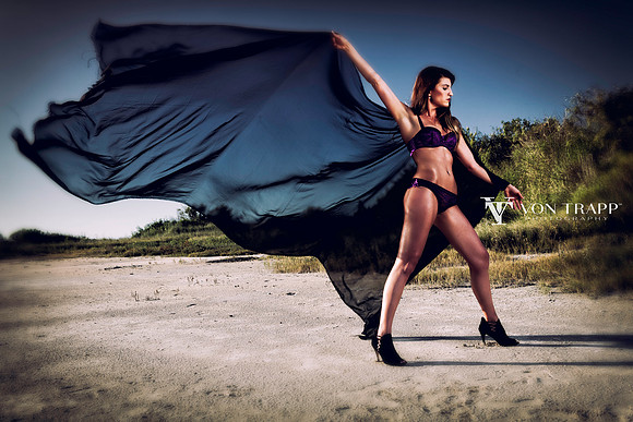 Sex fashion photo of a woman in lingerie on a beach holding black fabric in the wind.