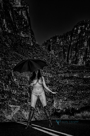 Fine art nude photo in B&W of a woman in thigh high boot, holding an umbrella, posed nude on a highway in west Texas.