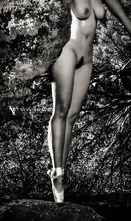 Art nude photo of a sexy woman wearing toe shoes, en pointe of a rock outdoors.