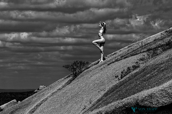Art nude photo of a woman standing on a stone hillside in the Texas desert.