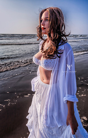 Glamout photo of a busty beauty in a white bra, sheer shirt, and skirt, posed on a Texas beach at sunrise.
