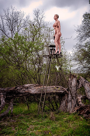 Art nude photo of a busty mature posed atop a deer stand with binoculars and wearing fuck me heels.