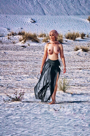 Art nude photo of a topless busty beauty in a sheer skirt and head scarf, walsing in the desert.