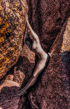 Color fine art nude photo of a woman posed intastingly between huge granite boulders, in the Texas hill country.