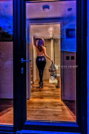Erotic voyeuristic boudoir photo of a partically nude woman, taking off her bra. As seen throw a glass door from nextdoor.