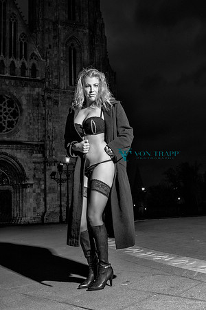 Lingerie glamour photo of a woman in a long coat flashing in front of a church in Budapest in the morning.