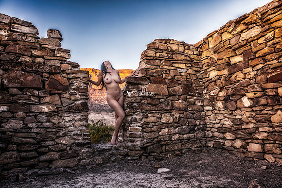 Color art nude photograph of a busty and leggy nude woman, posed in the doorway of a stone ruin building in the west Texas desert.