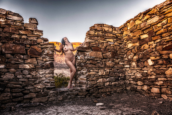 Color art nude photograph of a busty and leggy nude woman, posed in the doorway of a stone ruin building in the west Texas desert.
