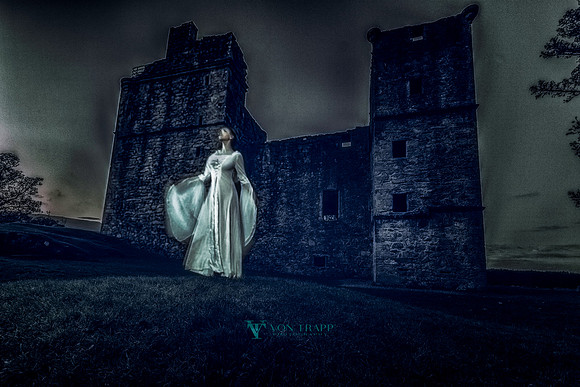Edgy and stylized color photo of a woman made to look like an apparition in front of a Scottish castle.