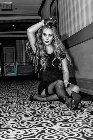 Photo of a sexy woman in a short dress, stockings and stilettoes, sitting on a hotel hallway floor.