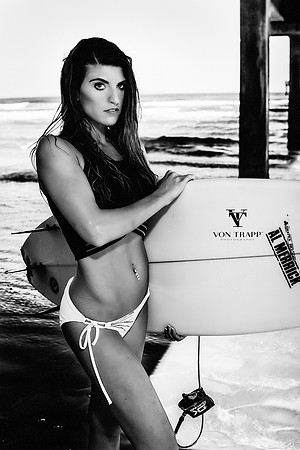 Glamour photo of a woman in a bathing suit under a pier in Texas, holding a surfboard.