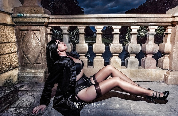 Fashion-Glamour photograph of a sexy raven haired woman in garter belt, stockings, bra, and long black coat, outdoors at a castle in Germany.