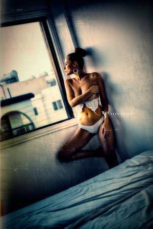 Fine art glamour image of a topless woman in lingerie at a hotel room window.