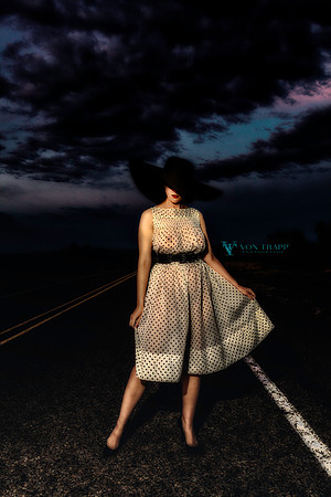 Glamour photo of a sexy woman in a sheer dress standing on a road.