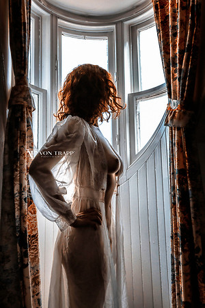 Glamour Fashion Boudoir photo of a busty semi-nude redhead in a sheer nightgown, standing in a dormer window in Scotland.