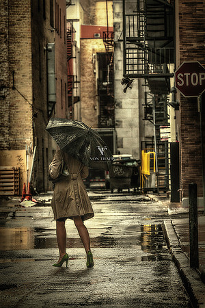 Edgy fine art fashion glamour photograph of woman in a trench coat, fishnet stockings and heels, striding down an ally on a rainy day holding an umbrella in San Antonio Texas.