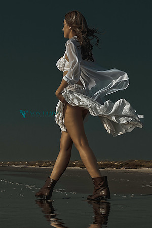 Fine art glamour photograph of a woman in a sheer white outfit on a beach.