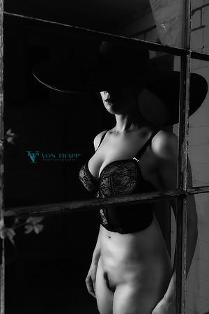 Hot fashion glamour photo of a seductive woman without panties, wearing a bustier and chapeau seen through a window.