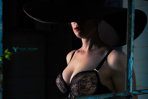 Hot fashion glamour photo of a seductive woman without panties, wearing a bustier and chapeau seen through a window.