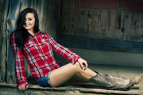 Glamour photo of a young woman in a play shirt short shorts and cowgirl boots.