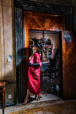 Sexy fashion photo of an elegant woman in a red robe, leather opera gloves and scrappy sandals taken in a Venetian palazzo.