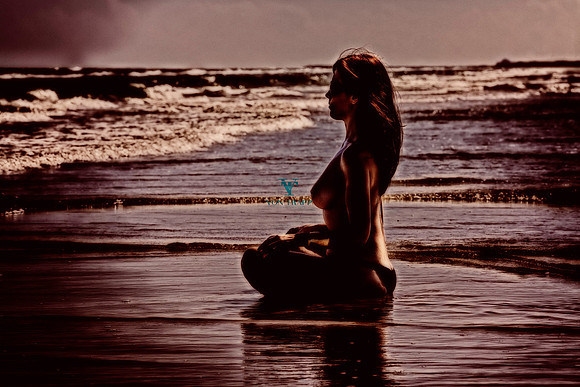 Art nude glamour photograph of a busty and topless woman sitting at the water's edge on a Texas beach.
