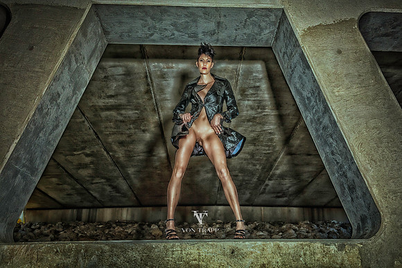 Hot fashion nude photo of a sexy woman wearing a long coat without panties, flashing under a bridge.