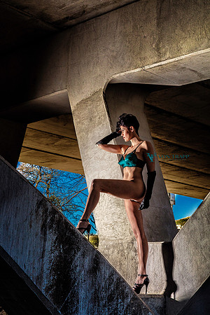 Sexy fashion nude of a woman in an emerald bullet bra under a bridge.