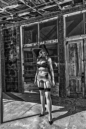 Black and white fashion-glamour photo of a hot woman outdoors in bra, garter belt, stockings ,broad brim hat and come fuck me stilettoes, flashing her pussy in public.
