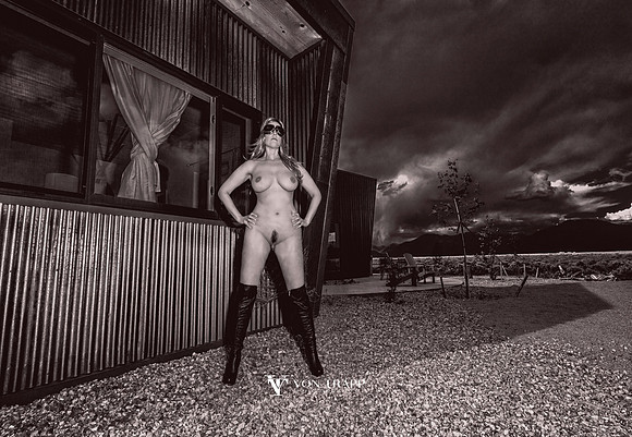 Photo of a nude woman in thigh high boots and aviator goggles, outdoors with a dramatic sky.