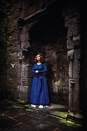 Fine art photo of a busty redhead wearing medieval clothing and a crown, standing in a castle fireplace in Scotland.
