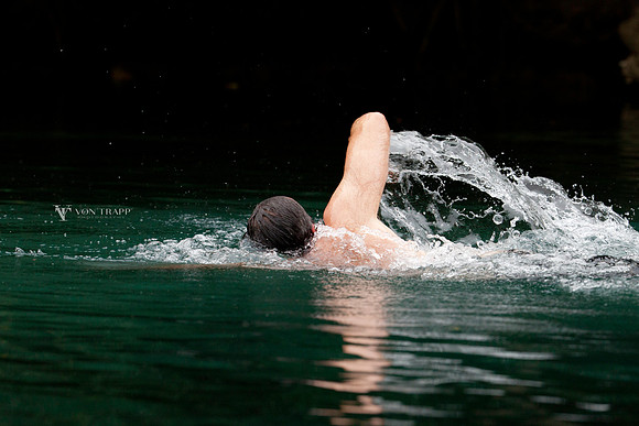 Lifestyle photograph of a young man swimming in a river.