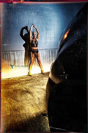 Edgy fashion photo of a busty woman in lingerie exposed in the headlights of a car.