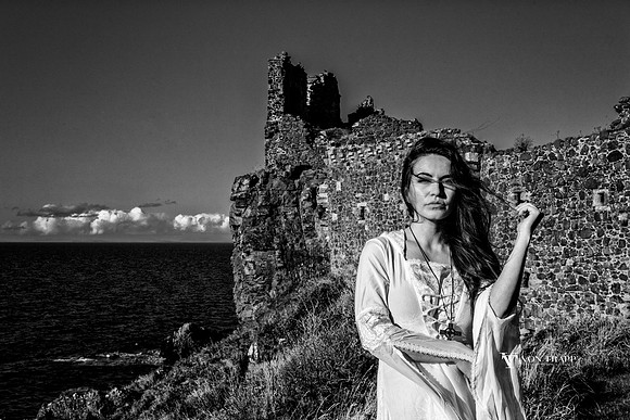 Glamour photo of a woman in a white Celtic dress  in front of a castle on the coast of Scotland.
