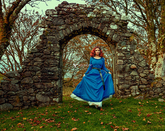 Period-inspired photo of a hot redhead in Celtic garb, outdoors by a Scottish castle.